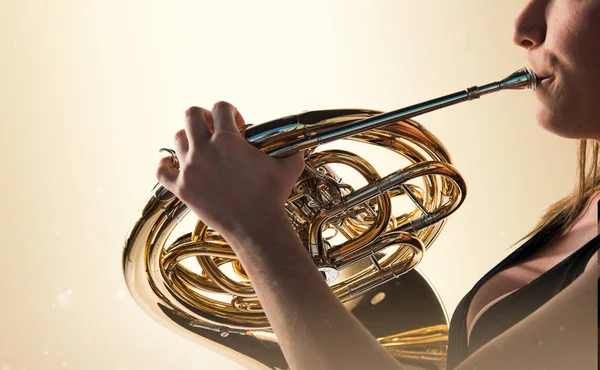 Chica tocando el cuerno francés sobre fondo ocre — Foto de Stock