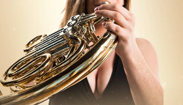 Girl playing the french horn on ocher background — Stock Photo, Image