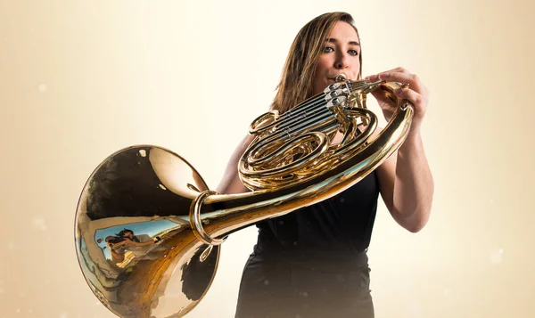 Chica tocando el cuerno francés sobre fondo ocre —  Fotos de Stock