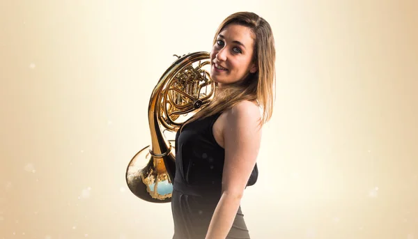 Girl playing the french horn on ocher background