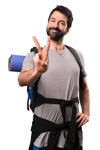 Przystojny backpacker podejmowania gest zwycięstwa na białym tle — Zdjęcie stockowe