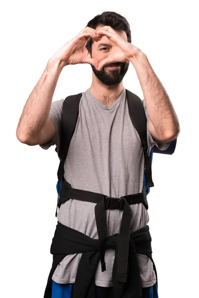 Handsome backpacker making a heart with his hands on white backg — Stock Photo, Image
