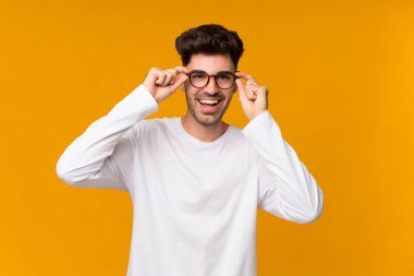 Genç adam turuncu arka planda gözlüklü ve şaşırmış.