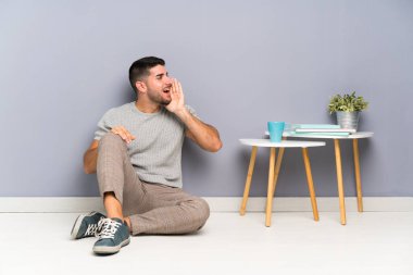 Genç yakışıklı adam yerde oturuyor ve ağzı açık bağırıyor.