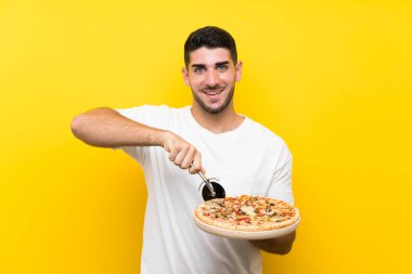 İzole sarı duvar üzerinde bir pizza tutan genç yakışıklı adam