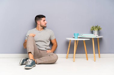 Genç yakışıklı adam yerde oturuyor, yan tarafa bakıyor.