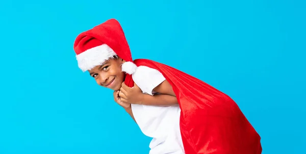 Menino afro-americano com chapéu de Natal e levando um saco com presentes — Fotografia de Stock