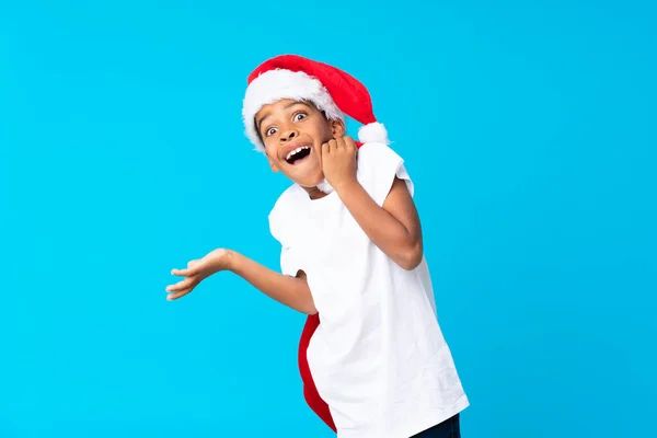 Chico afroamericano con sombrero de Navidad y tomar una bolsa con regalos haciendo gesto sorpresa —  Fotos de Stock