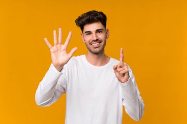 İzole edilmiş turuncu arka planı olan genç adam parmaklarıyla altısını sayıyor.