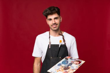 Soyutlanmış arka planda palet tutan genç bir adam.