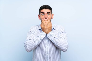 Kafkasyalı yakışıklı, yalıtılmış mavi arka planda, şaşırmış bir yüz ifadesi var.