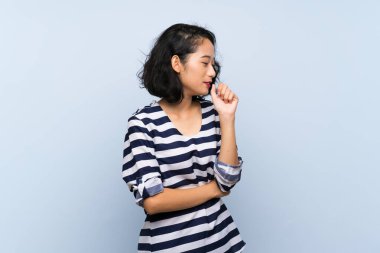 Asyalı genç bir kadın, izole edilmiş mavi arka planda öksürük ve kötü hislerle acı çekiyor.