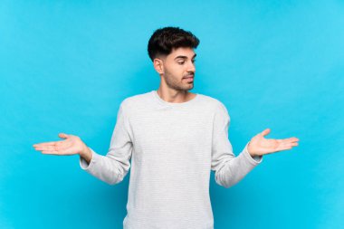 Tek başına mavi arka planı olan genç bir adam iki eliyle kopyalama alanını tutuyor.