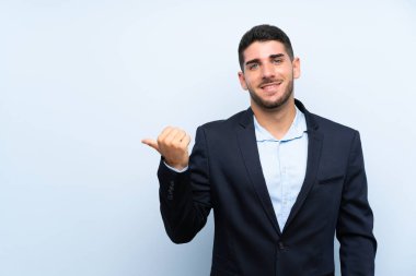 Soyutlanmış mavi arkaplan üzerinde yakışıklı bir adam bir ürün sunmak için kenarı işaret ediyor