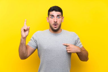 Sürpriz yüz ifadesi ile izole sarı arka plan üzerinde genç yakışıklı adam
