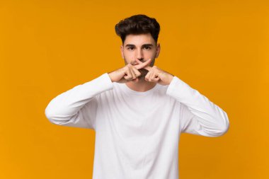 İzole edilmiş turuncu arka planda genç bir adam sessizlik işareti gösteriyor.
