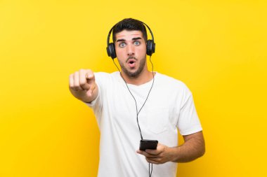 Genç yakışıklı adam müzik dinliyor. Seyyar, izole edilmiş sarı duvarı var. Şaşırmış ve öne bakıyor.