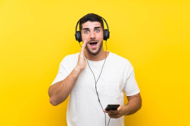 Müzik dinleyen genç yakışıklı bir adam. Seyyar, izole edilmiş sarı bir duvarı var. Şaşırmış ve şok olmuş bir yüz ifadesi var.