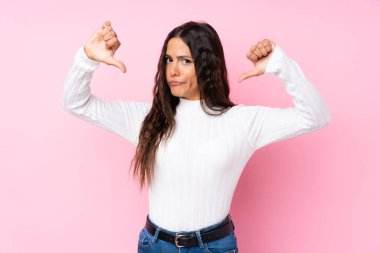 Soyutlanmış pembe arka planda genç bir kadın baş parmağını aşağı gösteriyor.