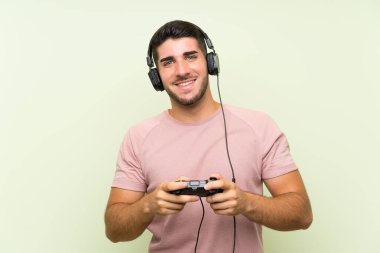 İzole yeşil duvar üzerinde bir video oyunu denetleyicisi ile oynayan genç yakışıklı adam
