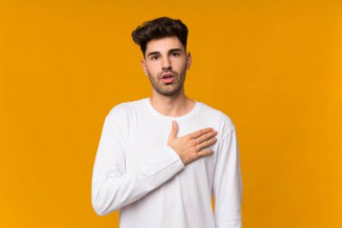 İzole edilmiş turuncu arka planı olan genç adam sağa bakarken şaşırmış ve şok olmuştu.