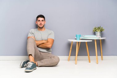 Genç yakışıklı adam kollarını kavuşturarak yerde oturuyor.