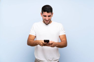 Kafkas yakışıklı adam izole mavi arka planda cep telefonuyla bir mesaj gönderiyor.
