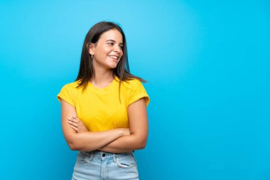 Genç kız mavi arka planda mutlu ve gülümsüyor.