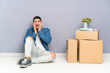 Yakışıklı genç adam sürpriz yüz ifadesi ile kutular arasında yeni evde hareket