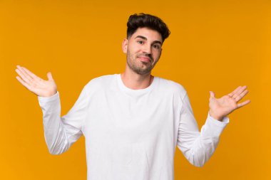 İzole edilmiş turuncu arka planı olan genç bir adam ellerini kaldırırken şüphe duyuyor.