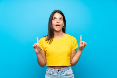 Soyutlanmış mavi arka planı olan genç bir kız şaşırmış ve yukarı bakıyor.