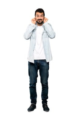 Sakallı, yakışıklı bir adamın uzun bir resmi. Hüsrana uğramış ve kulakları izole edilmiş beyaz arka planda.