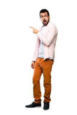 Sakallı, yakışıklı bir adam, beyaz arka planda şaşırmış ve işaret ediyor.