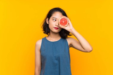 Genç asyalı kız izole turuncu arka plan üzerinde bir greyfurt tutan