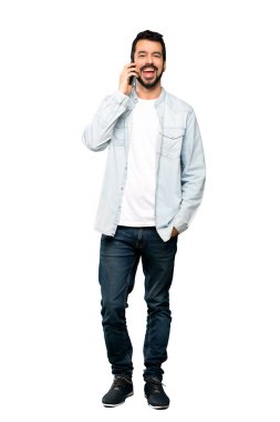 Sakallı, yakışıklı bir adamın izole edilmiş beyaz arka planda cep telefonuyla sohbet ederken tam boy görüntüsü.