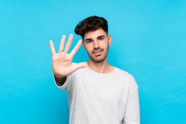 İzole edilmiş mavi arka plan üzerinde genç adam parmaklarıyla beşi sayıyor