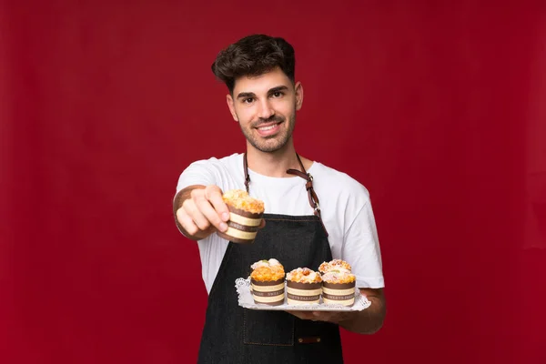 Joven Sobre Fondo Aislado Sosteniendo Mini Pasteles Ofreciéndolo — Foto de Stock