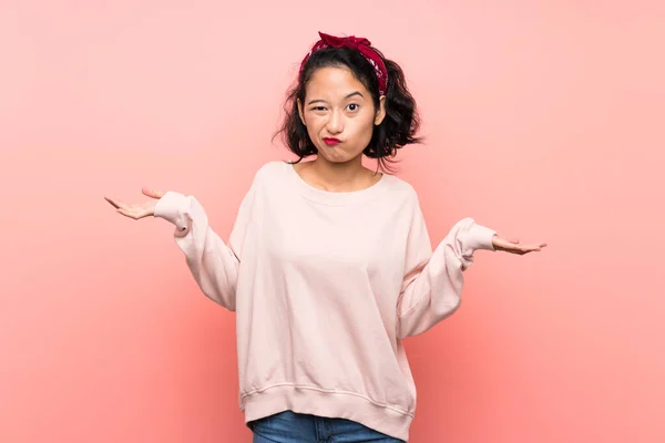 亚洲年轻女子 身披粉色背景 举手表决时疑虑重重 — 图库照片