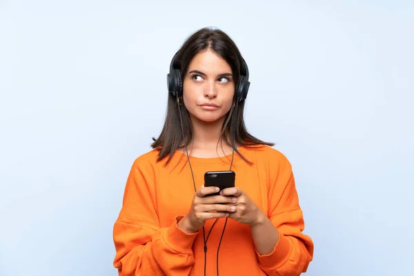 Jeune femme écoutant de la musique avec un mobile sur un mur bleu isolé — Photo