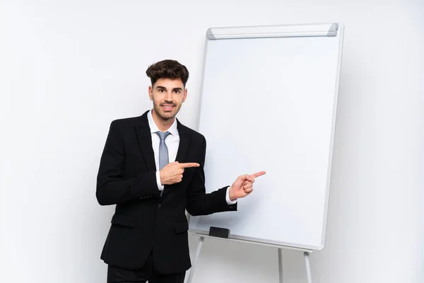 Young businessman giving a presentation on white board surprised and pointing side