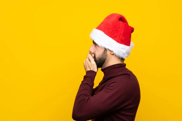 Человек Рождественской Шляпе Изолированном Жёлтом Фоне Закрывающий Рот Смотрящий Сторону — стоковое фото
