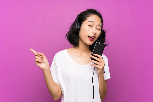 Asiática joven escuchando música con un móvil y cantando sobre aislada pared púrpura — Foto de Stock
