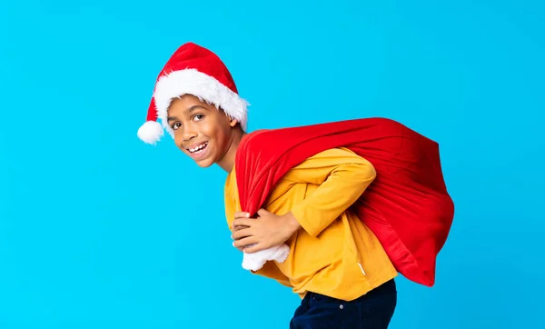 Niño afroamericano con sombrero de navidad y llevando una bolsa con regalos — Foto de Stock