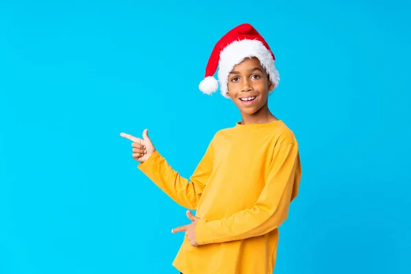 戴着圣诞礼帽的非裔美国男孩惊讶地指着旁边 — 图库照片