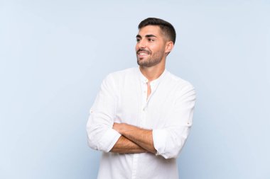 Sakallı yakışıklı bir adam mavi arka planda mutlu ve gülümsüyor.