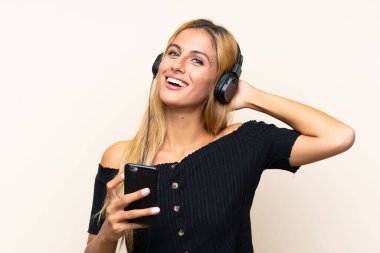 Genç sarışın kadın izole arka plan üzerinde bir cep telefonu ile müzik dinliyor