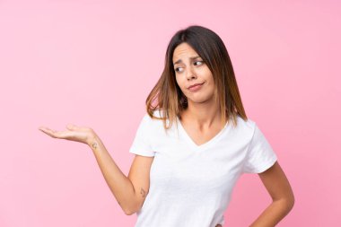 İzole edilmiş pembe arka plan üzerinde genç bir kadın kopyalama alanını kuşkularla dolduruyor