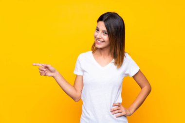 İzole edilmiş sarı arka planda genç bir kadın parmak işareti yapıyor.