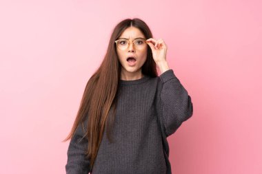 Gözlüklü ve şaşırmış pembe arka planı olan genç bir kadın.