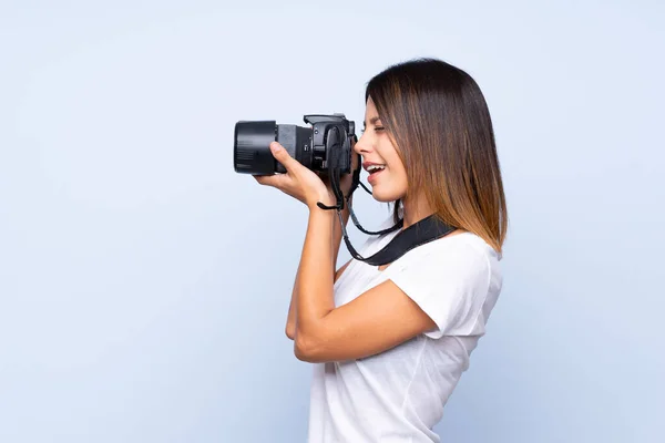 Mujer Joven Sobre Fondo Azul Aislado Con Una Cámara Profesional — Foto de Stock